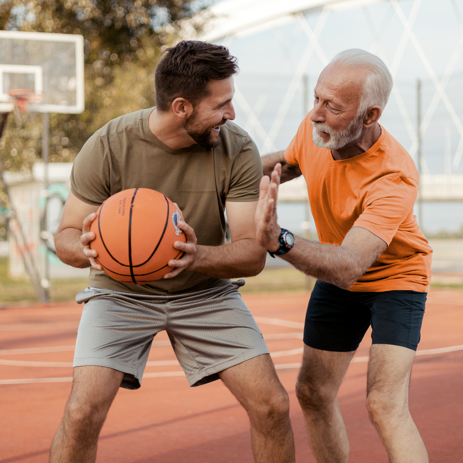 Zwei Männer spielen Basketball. Einer von ihnen ist jung, der andere etwas älter. Der junge Mann hält den Basketball in beiden Händen. | VIACTIV Krankenkasse