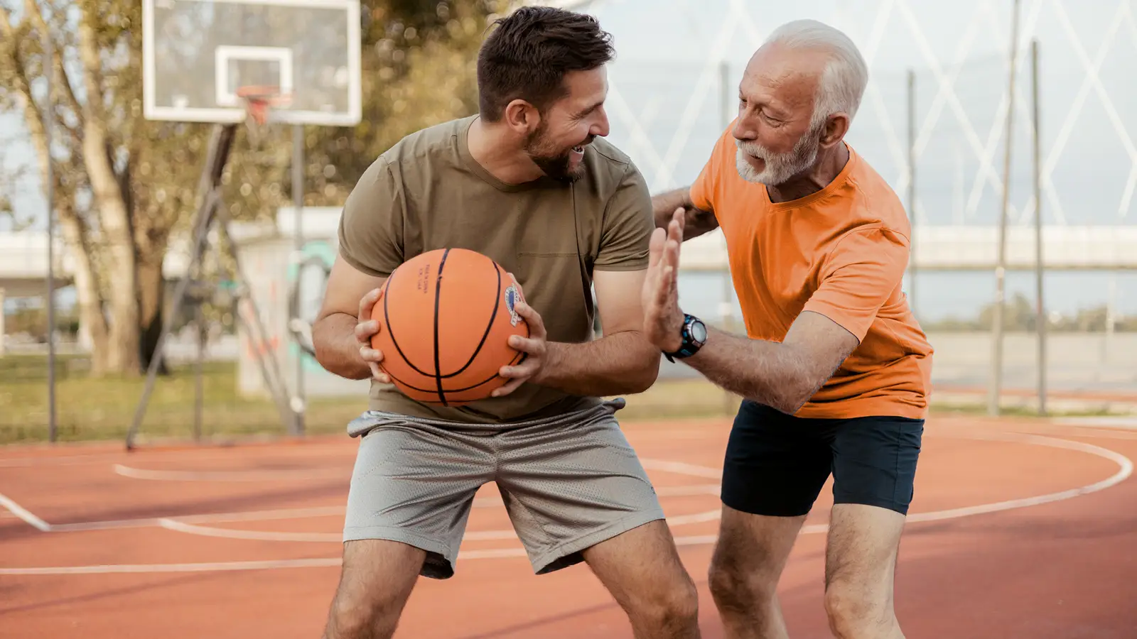 Zwei Männer spielen Basketball. Einer von ihnen ist jung, der andere etwas älter. Der junge Mann hält den Basketball in beiden Händen. | VIACTIV Krankenkasse