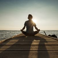 Joyful man meditating on pontoon over a lake at sunrise | VIACTIV Krankenkasse