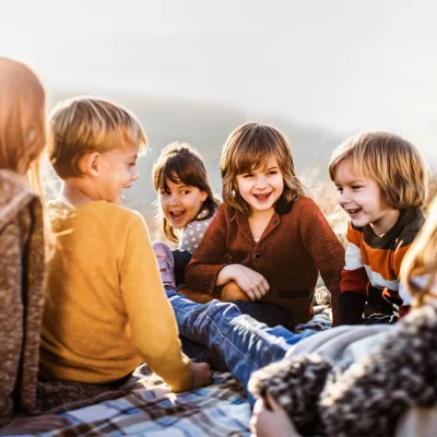 Eine Gruppe junger Kinder sitzt gemeinsam draußen auf einer Decke. | VIACTIV Krankenkasse