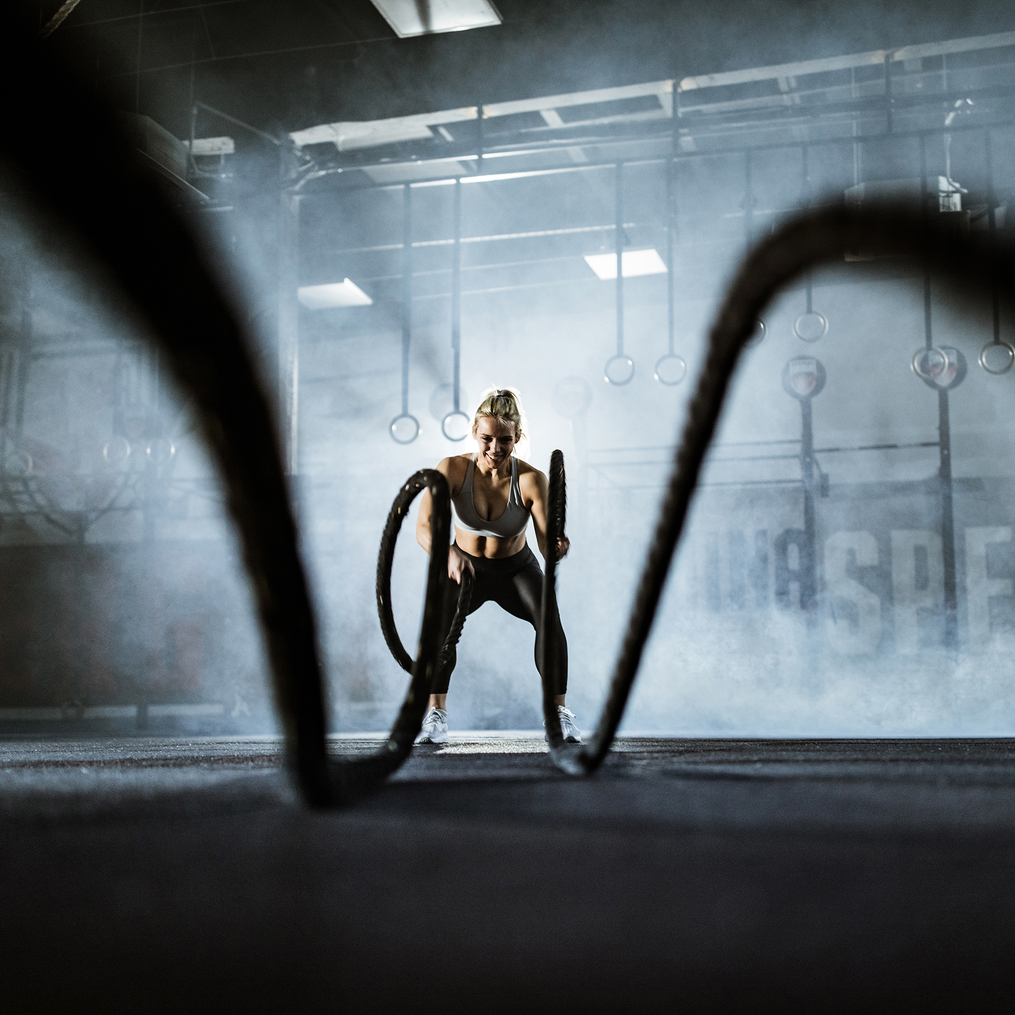 Happy female athlete exercising with battle ropes in a gym. | VIACTIV Krankenkasse