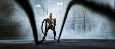 Happy female athlete exercising with battle ropes in a gym. | VIACTIV Krankenkasse