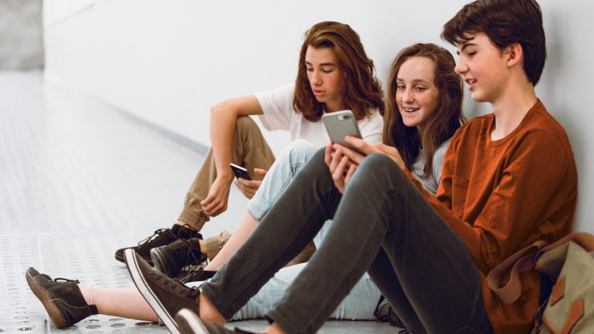 Drei Jugendliche sitzen nebeneinander auf dem Boden und schauen in ihre Handys. | VIACTIV Krankenkasse