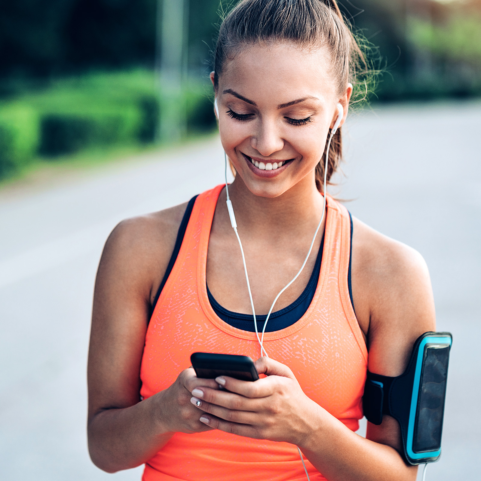 Eine Frau hat Kopfhörer in den Ohren und ist bereit joggen zu gehen. Sie startet die Musik an dem Telefon. | VIACTIV Krankenkasse