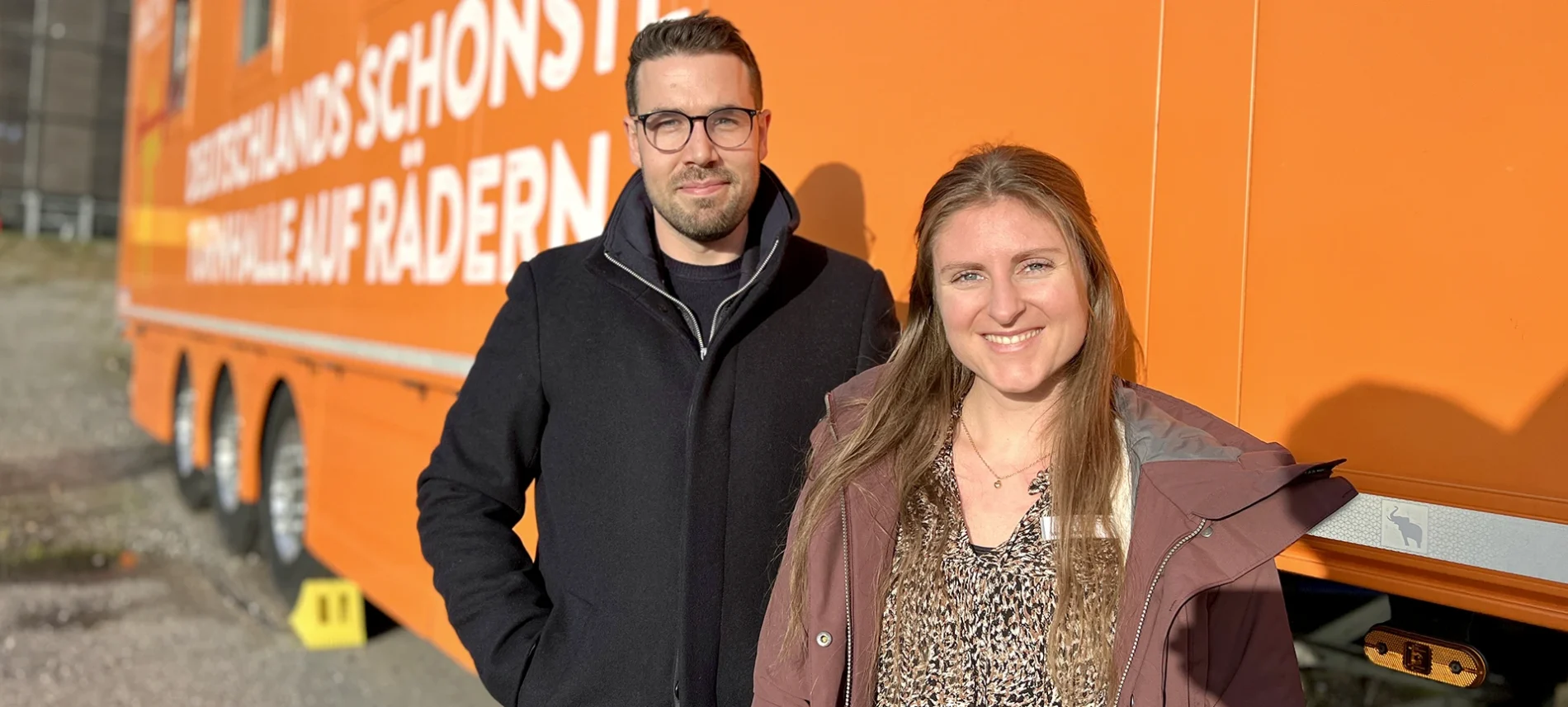 Zwei Mitarbeitende der VIACTIV stehen vor dem Fitness-Truck der VIACTIV Krankenkasse und lächeln in die Kamera. | VIACTIV Krankenkasse