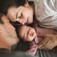 Close up of young father and mother lying on bed and looking at their newborn baby at home. | VIACTIV Krankenkasse