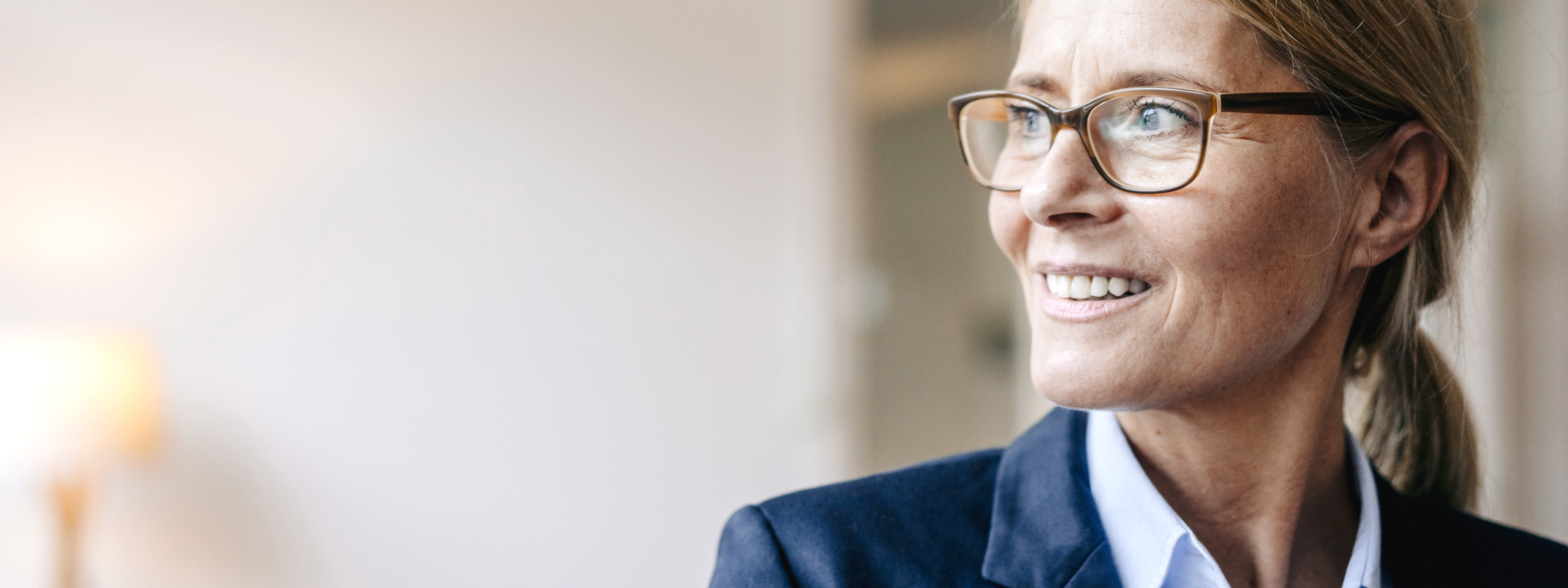 Eine Frau mittleren Alters im Business-Outfit schaut gut gelaunt in die Ferne. | VIACTIV Krankenkasse