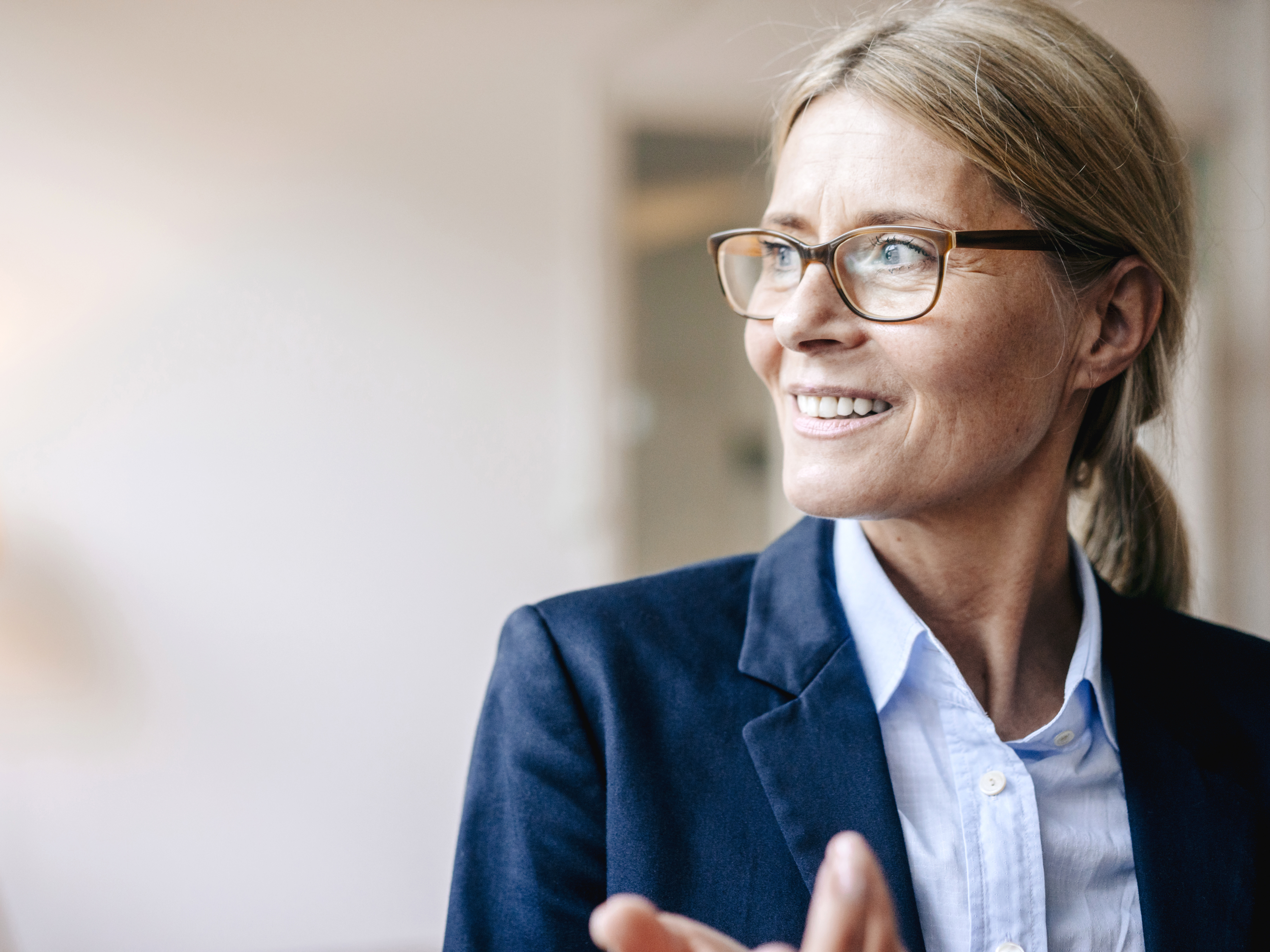 Eine Frau mittleren Alters im Business-Outfit schaut gut gelaunt in die Ferne. | VIACTIV Krankenkasse