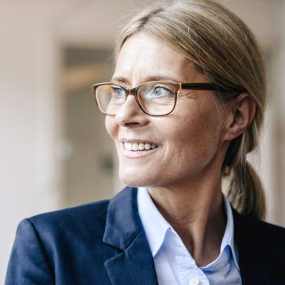 Eine Frau mittleren Alters im Business-Outfit schaut gut gelaunt in die Ferne. | VIACTIV Krankenkasse