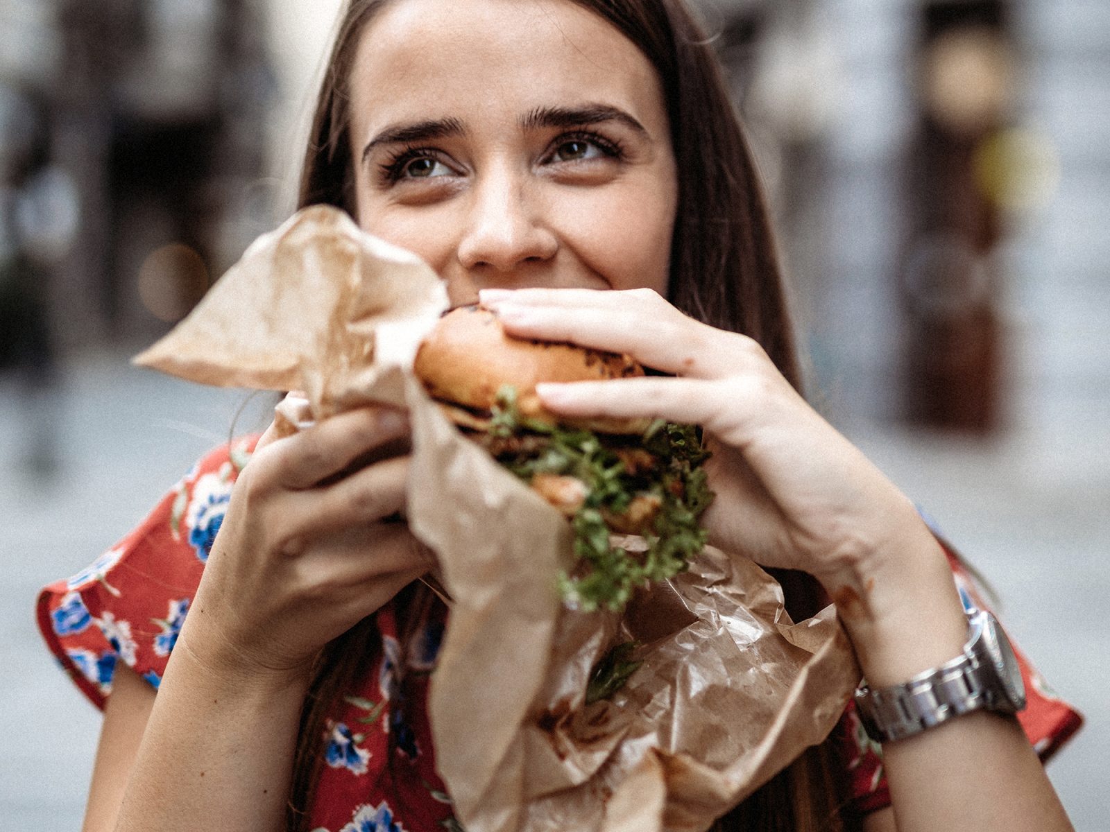 Eine junge Frau beißt genüsslich in ihren Burger. | VIACTIV Krankenkasse