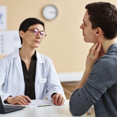 Ein Mann kratzt sich aufgrund einer Allergie beim Arzt am Hals. | VIACTIV Krankenkasse