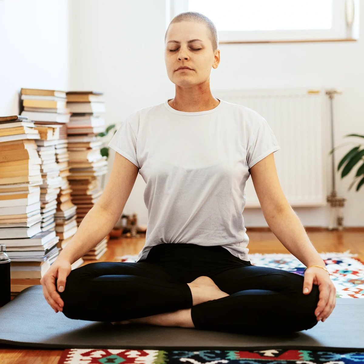 Junge Frau macht Yoga. Hohe Bücherstapel liegen im Hintergrund. | VIACTIV Krankenkasse