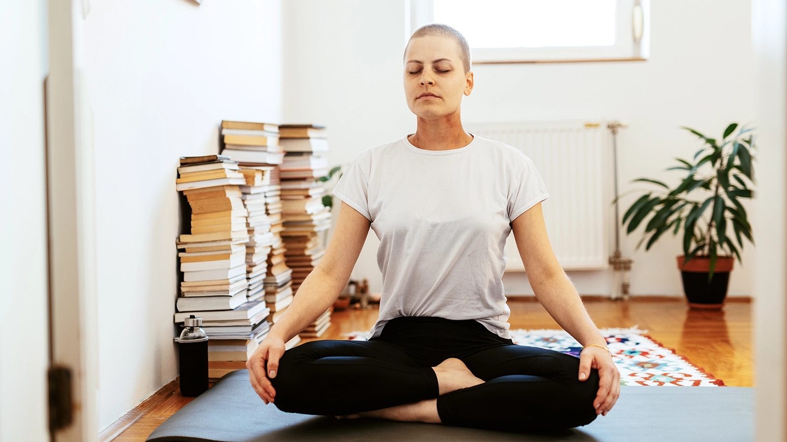 Junge Frau macht Yoga. Hohe Bücherstapel liegen im Hintergrund. | VIACTIV Krankenkasse
