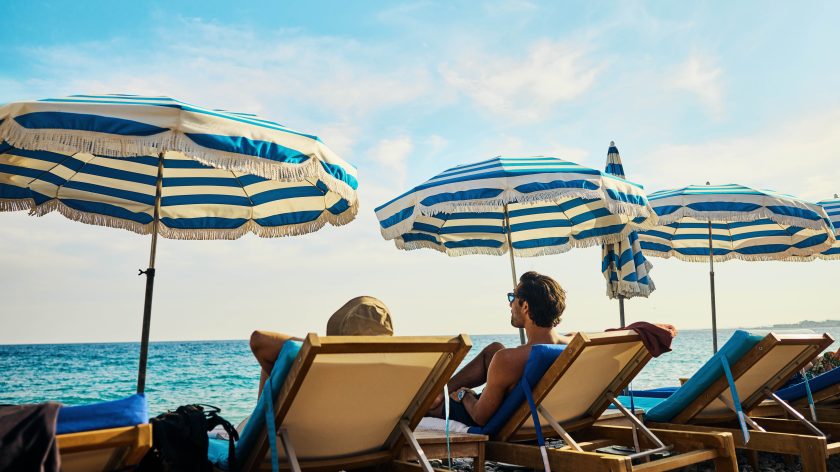 Zwei Menschen sitzen auf Liegestühlen unter Sonnenschirmen am Strand. | VIACTIV Krankenkasse