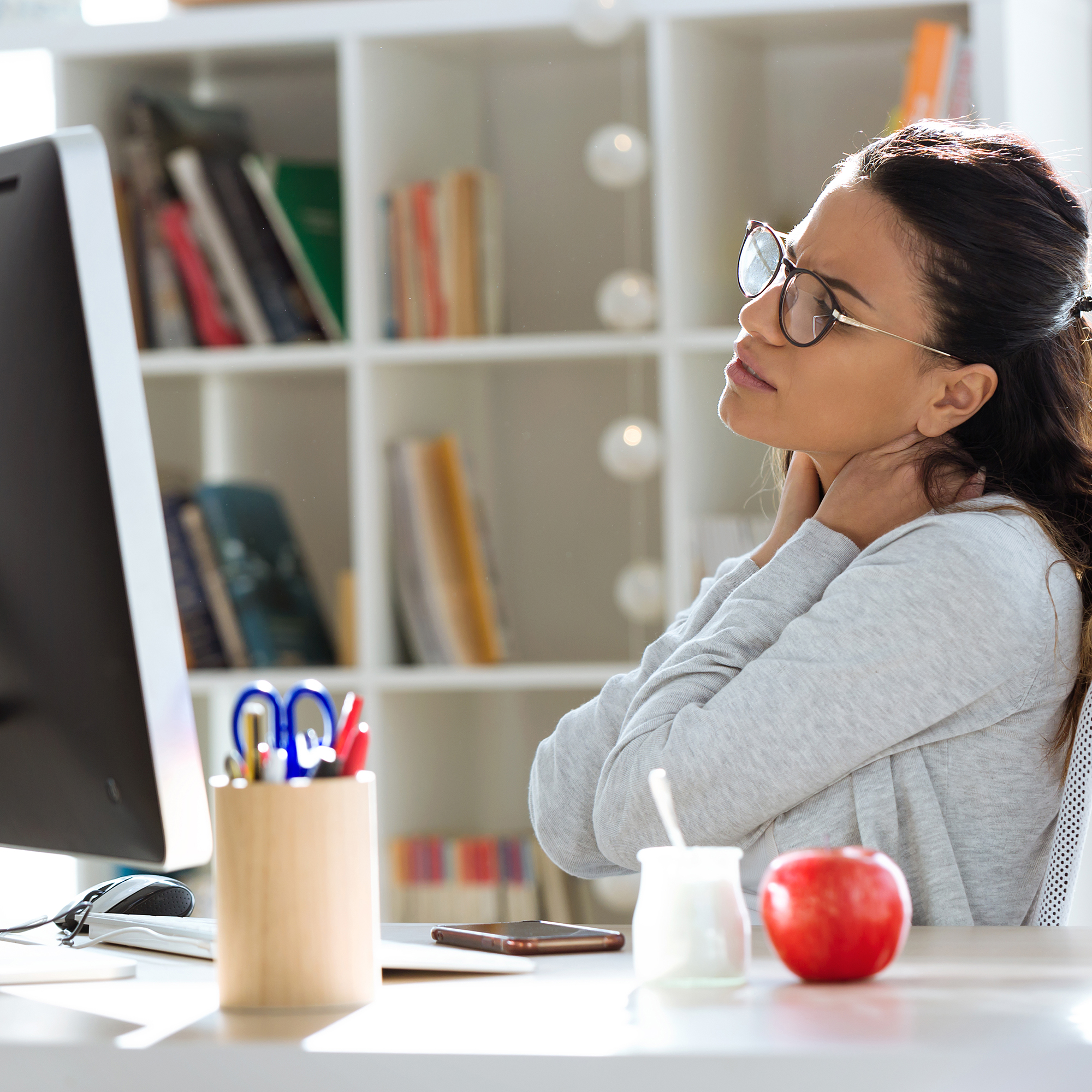 Tired young business woman having neck and back pain while working with computer in the office. | VIACTIV Krankenkasse