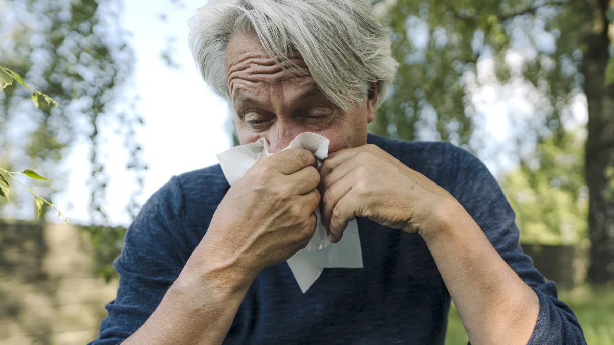 Ein älterer Mann putzt sich die Nase aufgrund einer Allergie. | VIACTIV Krankenkasse