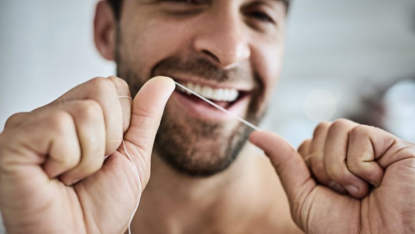 Junger Mann spannt Zahnseide zwischen seinen Fingern, um damit seine Zähne zu reinigen. | VIACTIV Krankenkasse