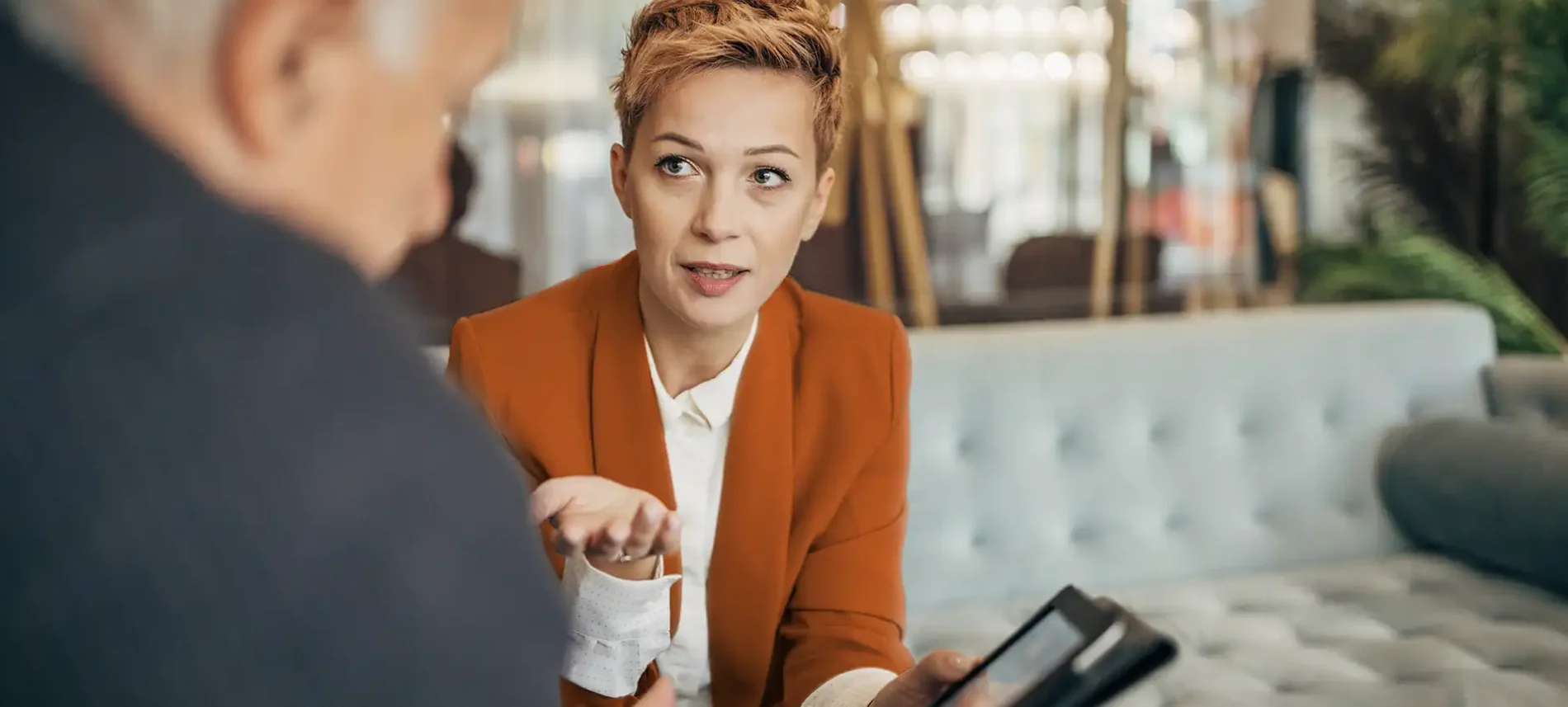 Eine Frau sitzt auf dem Sofa. Ihr gegenüber sitzt ein älterer Mann, mit dem sie sich unterhält. | VIACTIV Krankenkasse