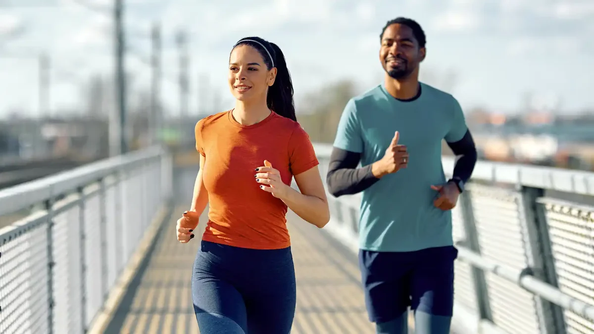 Eine junge Frau und ein junger Mann joggen gemeinsam über eine Brücke. | VIACTIV Krankenkasse