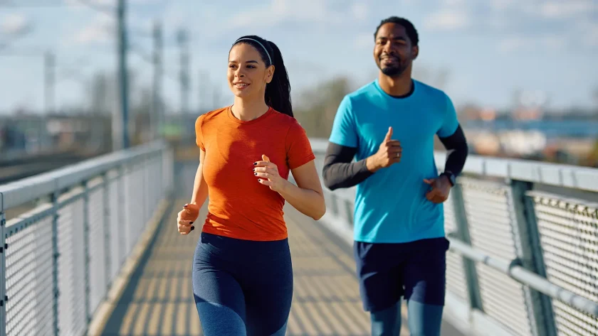 Zwei Personen joggen über eine Brücke. Die Sonne scheint und beide lächeln. | VIACTIV Krankenkasse