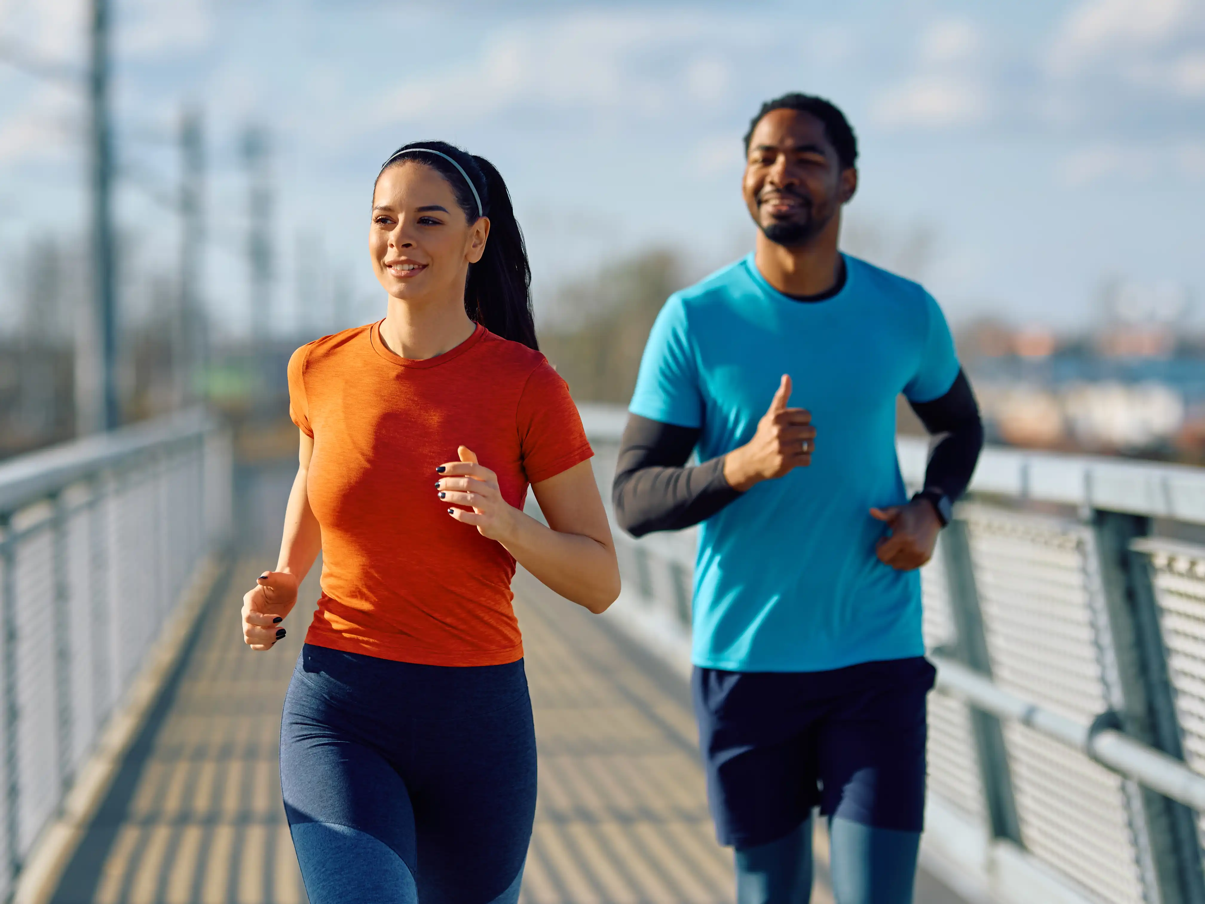 Eine junge Frau und ein junger Mann joggen gemeinsam über eine Brücke. | VIACTIV Krankenkasse
