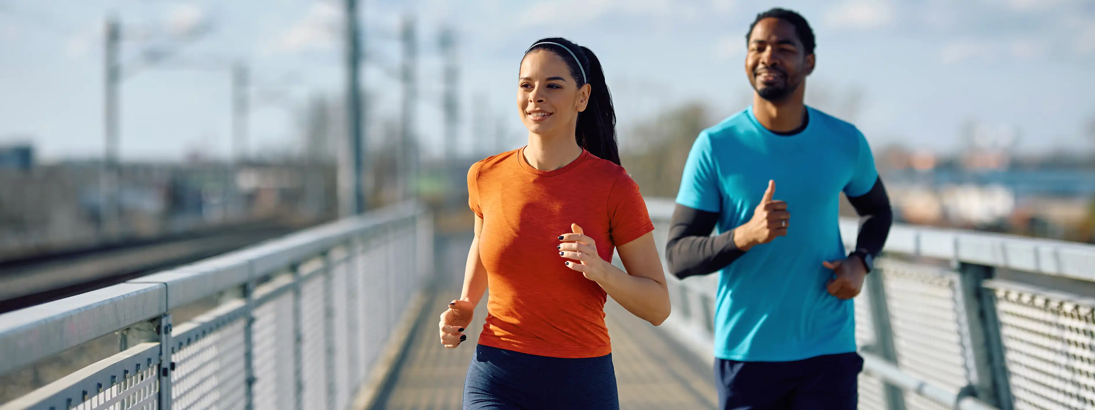 Eine junge Frau und ein junger Mann joggen gemeinsam über eine Brücke. | VIACTIV Krankenkasse