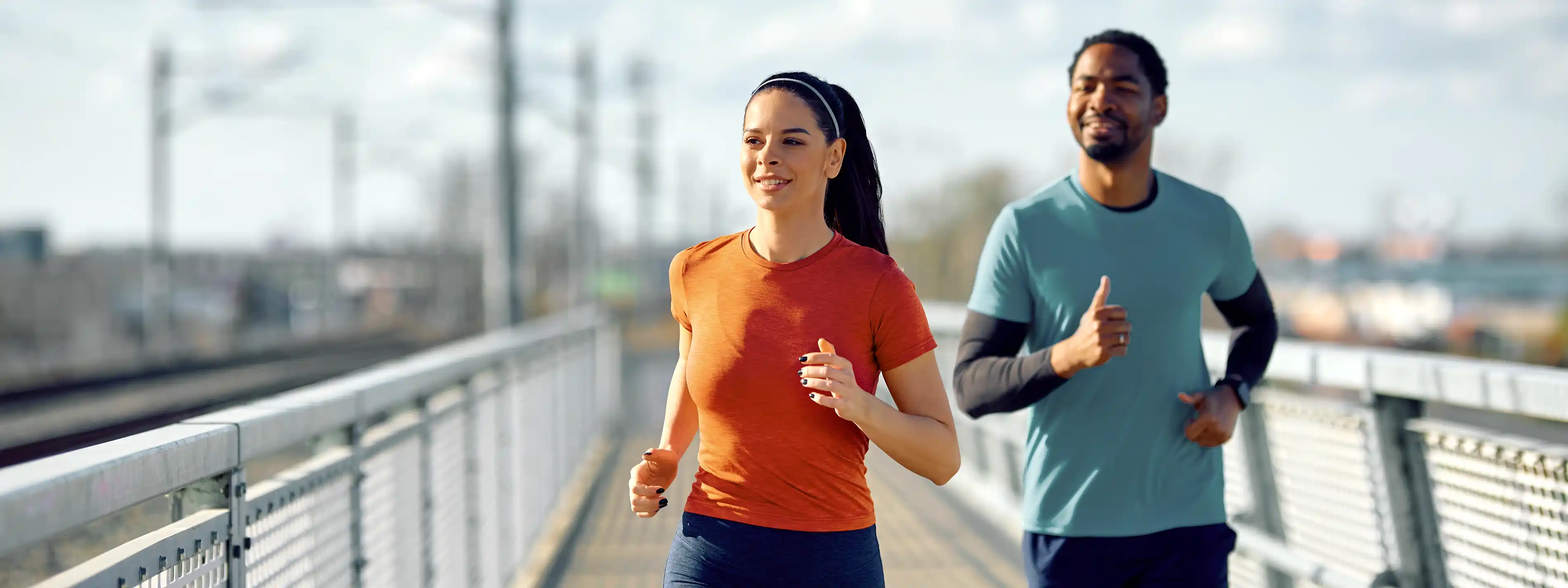 Eine junge Frau und ein junger Mann joggen gemeinsam über eine Brücke. | VIACTIV Krankenkasse