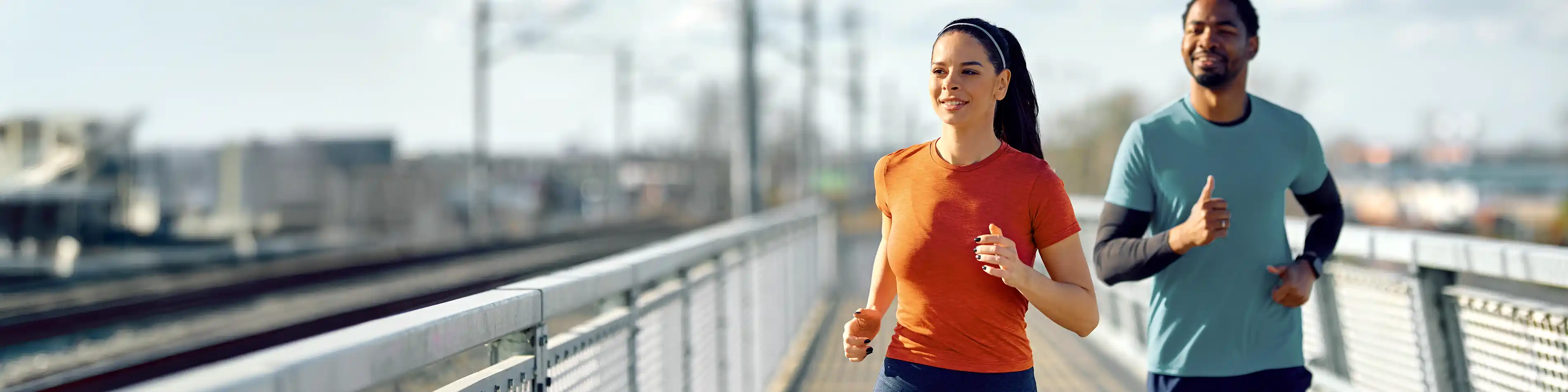 Eine junge Frau und ein junger Mann joggen gemeinsam über eine Brücke. | VIACTIV Krankenkasse