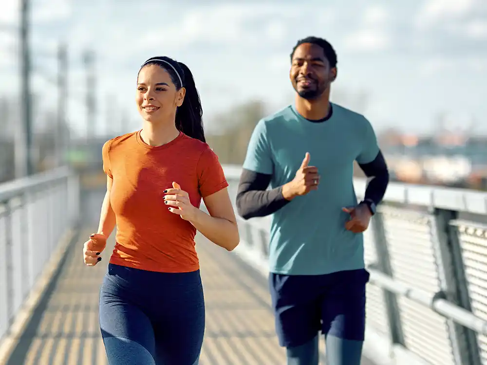 Eine junge Frau und ein junger Mann joggen gemeinsam über eine Brücke. | VIACTIV Krankenkasse