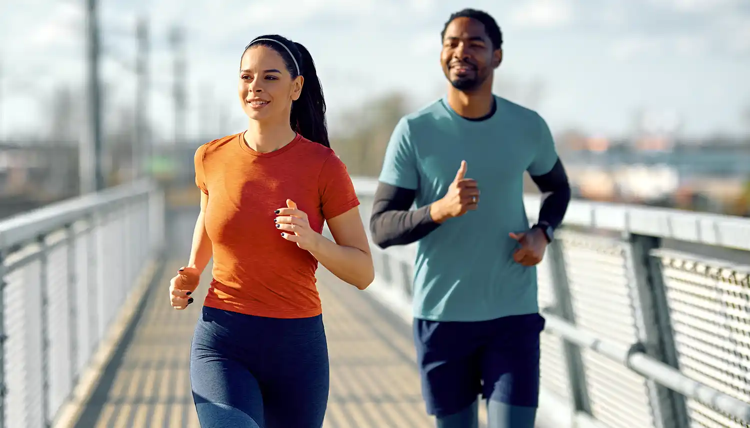 Eine junge Frau und ein junger Mann joggen gemeinsam über eine Brücke. | VIACTIV Krankenkasse