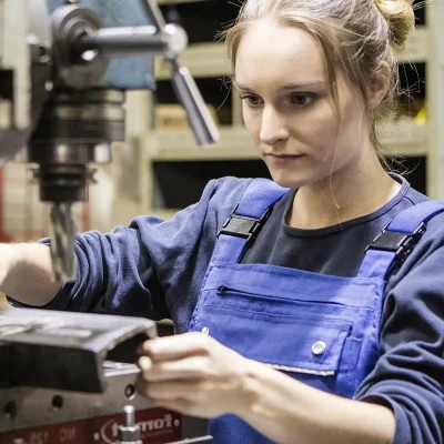 Eine Auszubildende steht an einer Maschine in einer Werkstatt und sieht konzentriert aus. | VIACTIV Krankenkasse