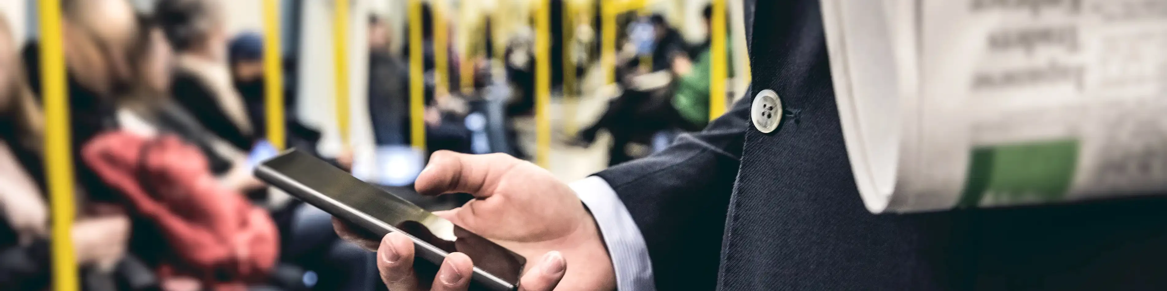 Ein Mann im Business-Anzug steht in der Bahn und schaut auf sein Handy. | VIACTIV Krankenkasse