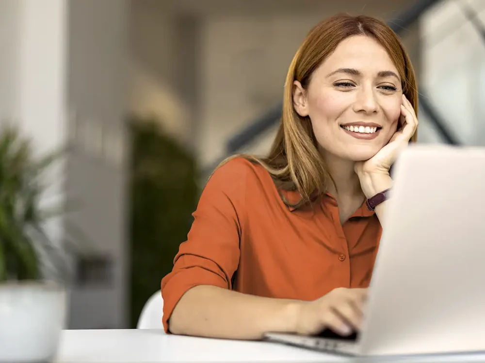 Eine Frau sitzt vor dem Laptop und schaut sich interessiert etwas an. | VIACTIV Krankenkasse