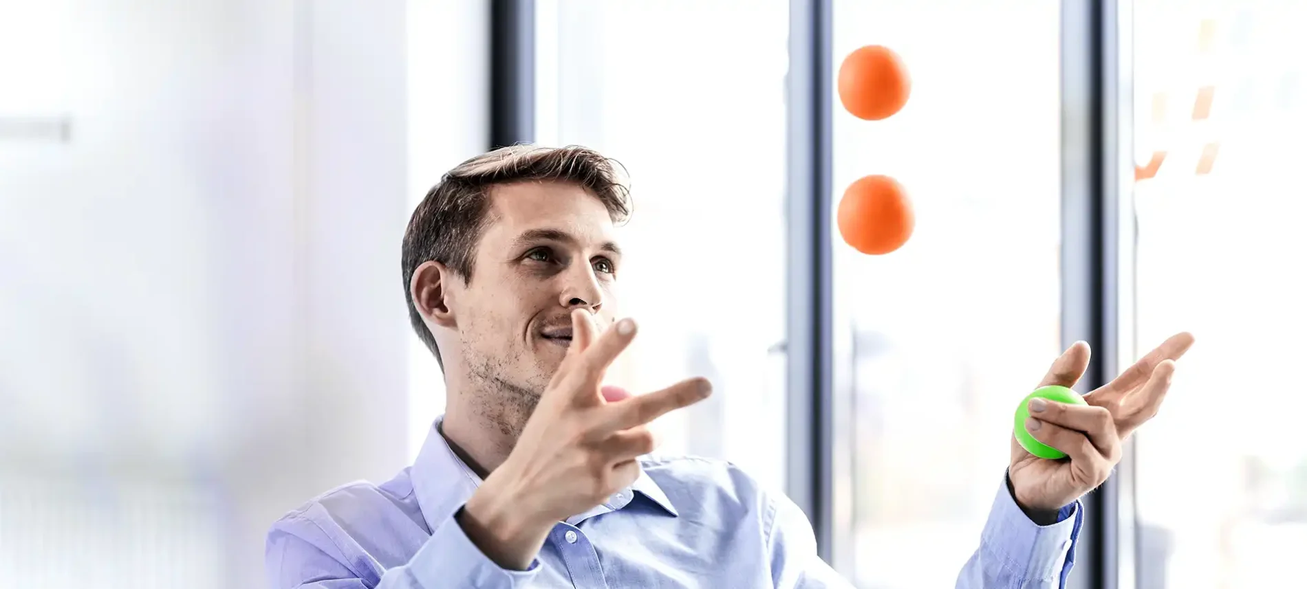 Ein Mann im Büro jongliert mit drei Bällen. Er wirkt konzentriert. | VIACTIV Krankenkasse