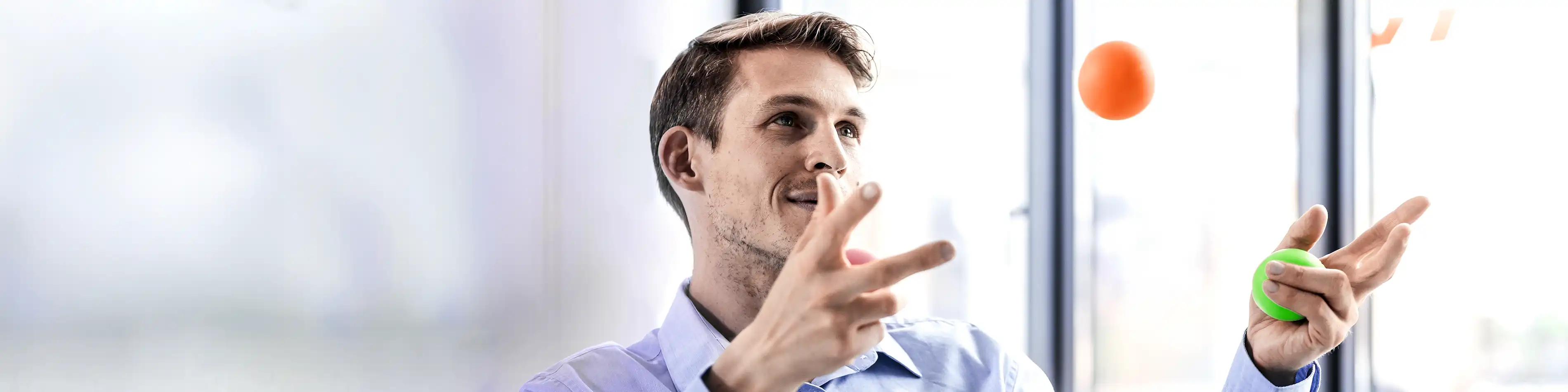Ein Mann im Büro jongliert mit drei Bällen. Er wirkt konzentriert. | VIACTIV Krankenkasse