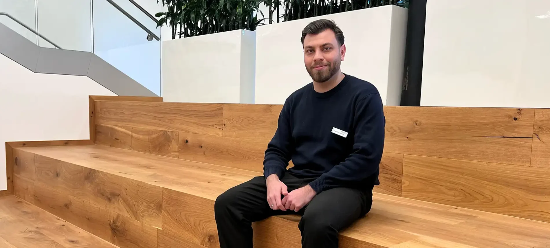 Mitarbeiter Umut Musa Bolten sitzt auf einer Holztreppe im Gebäude der VIACTIV. | VIACTIV Krankenkasse