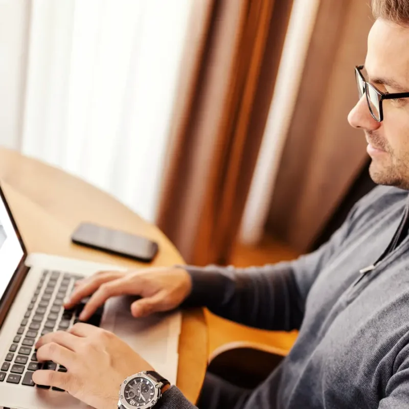 Ein Mann sitzt am Tisch und hat dort einen Laptop und ein Smartphone liegen. | VIACTIV Krankenkasse
