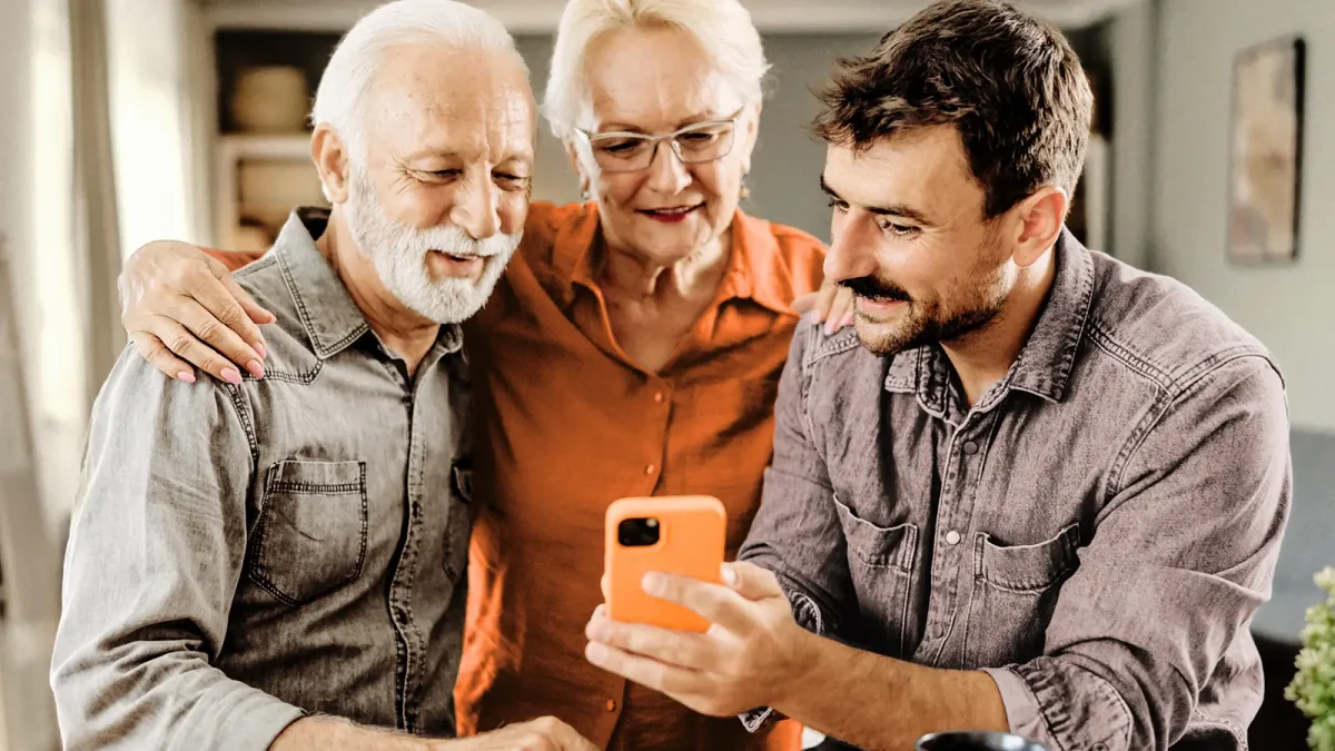 Zwei Männer und eine Frau stehen nebeneinander und gucken interessiert auf ein Smartphone | VIACTIV Krankenkasse