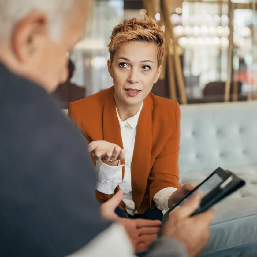 Eine Frau sitzt auf dem Sofa. Ihr gegenüber sitzt ein älterer Mann, mit dem sie sich unterhält. | VIACTIV Krankenkasse