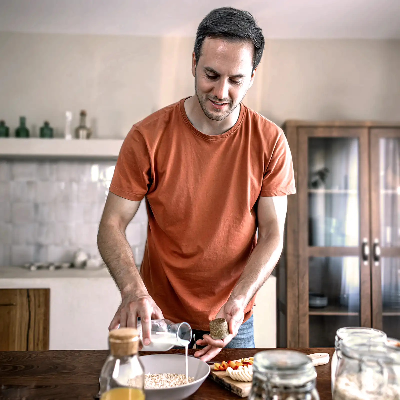 Ein Mann mit orangenem T-Shirt macht sich ein Müsli mit Milch und frischen Früchten. | VIACTIV Krankenkasse