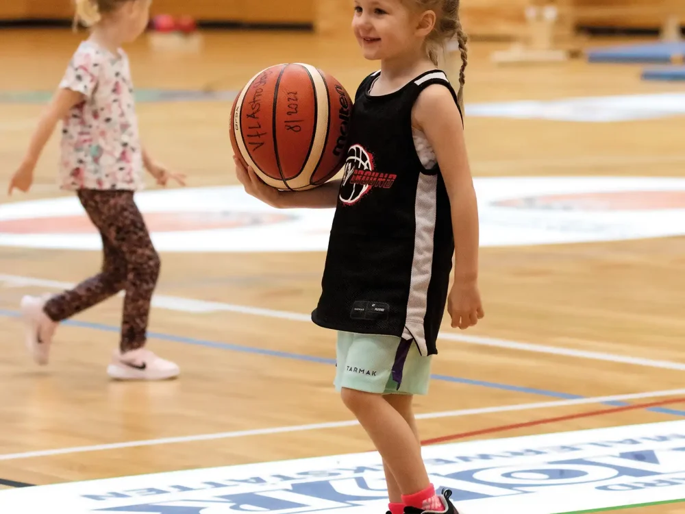 Ein kleines Mädchen hält einen Basketball in der Hand. Sie lacht. | VIACTIV Krankenkasse