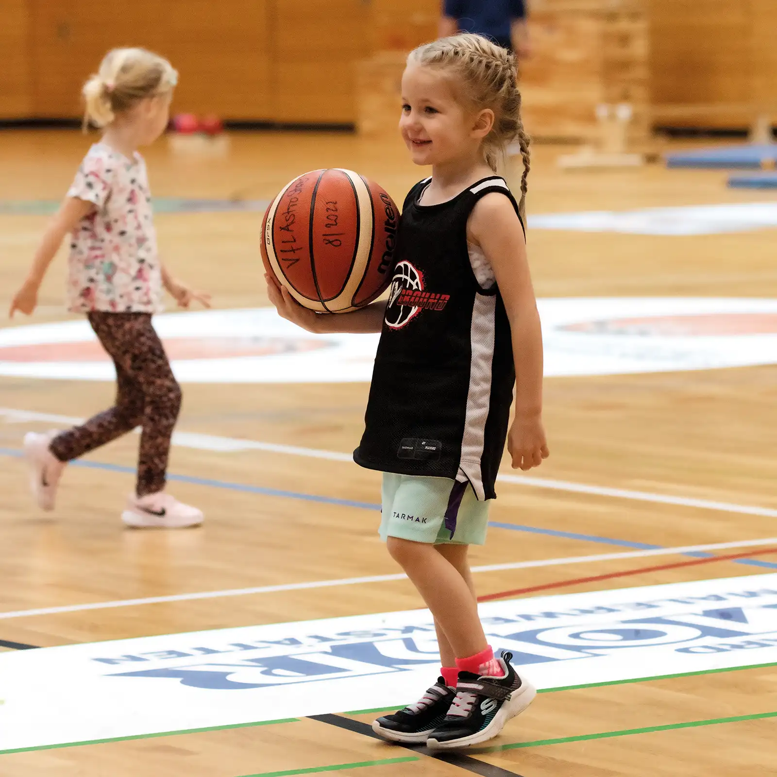 Ein kleines Mädchen hält einen Basketball in der Hand. Sie lacht. | VIACTIV Krankenkasse