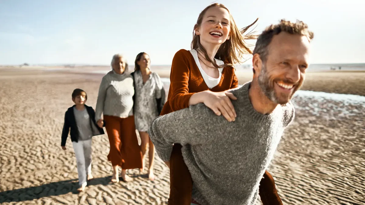 Eine Familie macht einen Ausflug am Strand. Sie sehen glücklich aus. | VIACTIV Krankenkasse