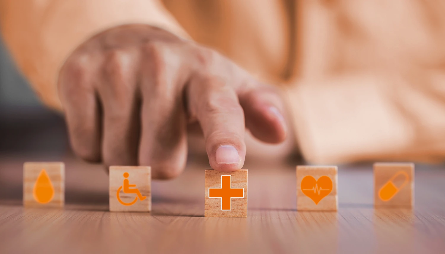 Fünf kleine Holzwürfel mit unterschiedlichen Symbolen wie Herz, Tablette und Rollstuhlfahrer liegen auf einem Tisch. | VIACTIV Krankenkasse