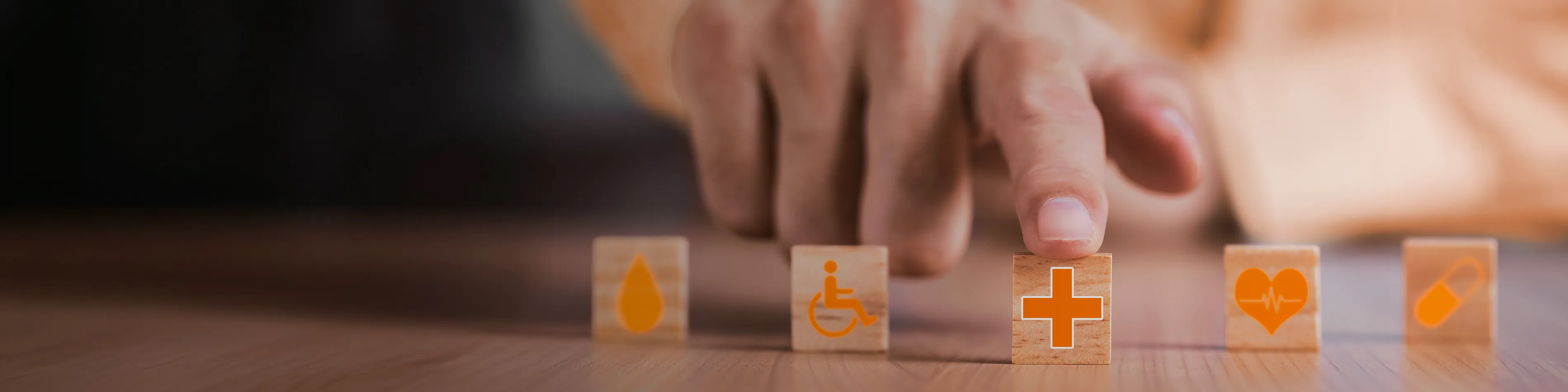 Fünf kleine Holzwürfel mit unterschiedlichen Symbolen wie Herz, Tablette und Rollstuhlfahrer liegen auf einem Tisch. | VIACTIV Krankenkasse