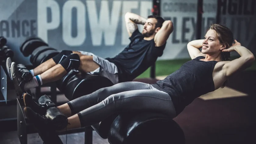 Eine Frau und ein Mann sind im Fitnessstudio und machen dort Sit-ups. | VIACTIV Krankenkasse