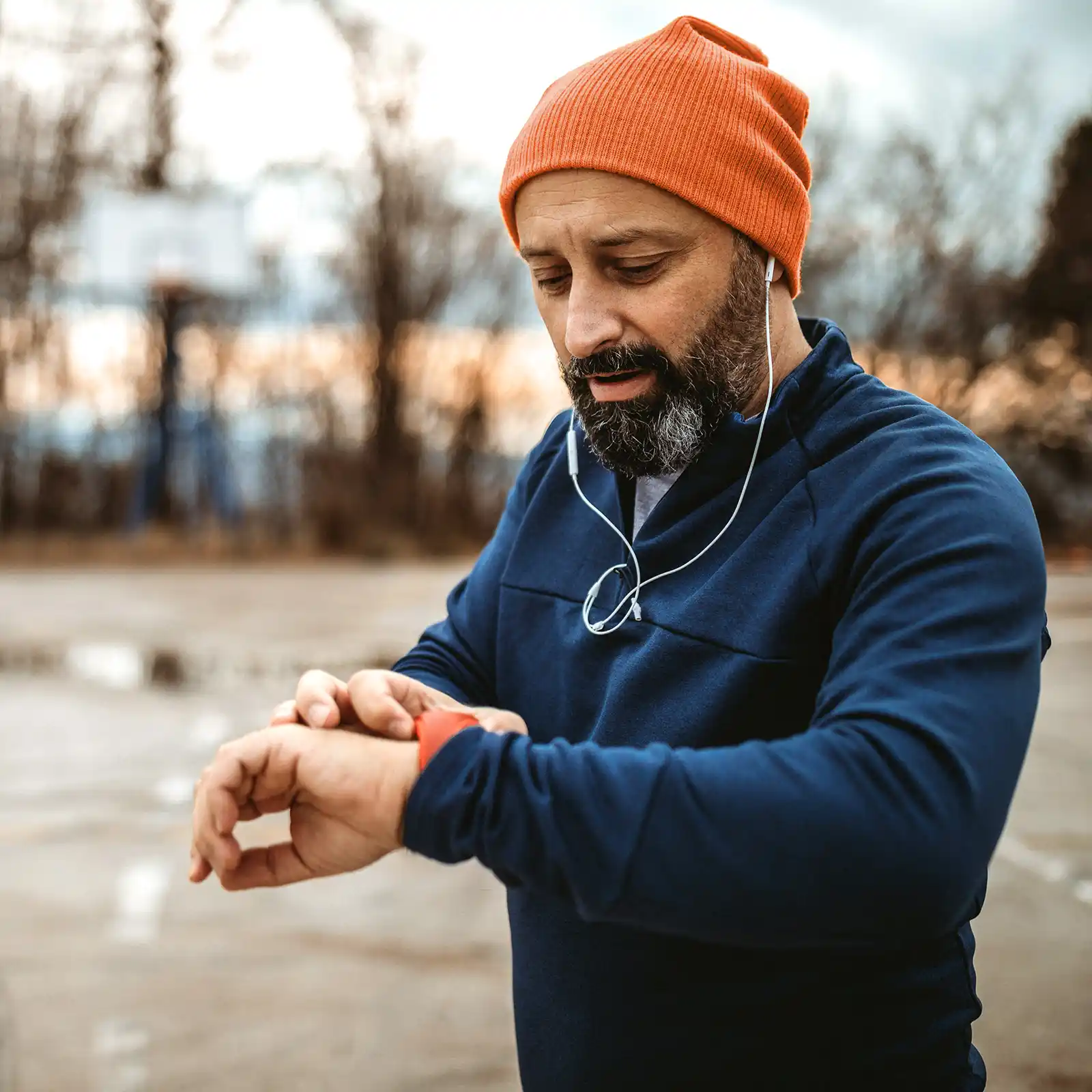 Ein Mann in Sportkleidung schaut auf seine Sportuhr und stoppt die Zeit seiner Joggingrunde. | VIACTIV Krankenkasse