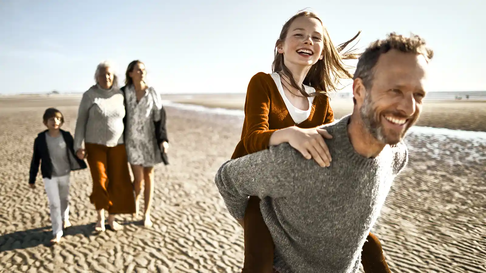 Eine Familie macht einen Ausflug am Strand. Sie sehen glücklich aus. | VIACTIV Krankenkasse