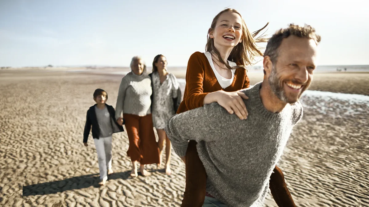 Eine Familie macht einen Ausflug am Strand. Sie sehen glücklich aus. | VIACTIV Krankenkasse