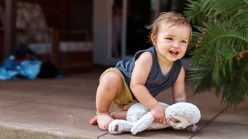 Ein Baby sitzt mit seinem Kuscheltier auf dem Boden. | VIACTIV Krankenkasse